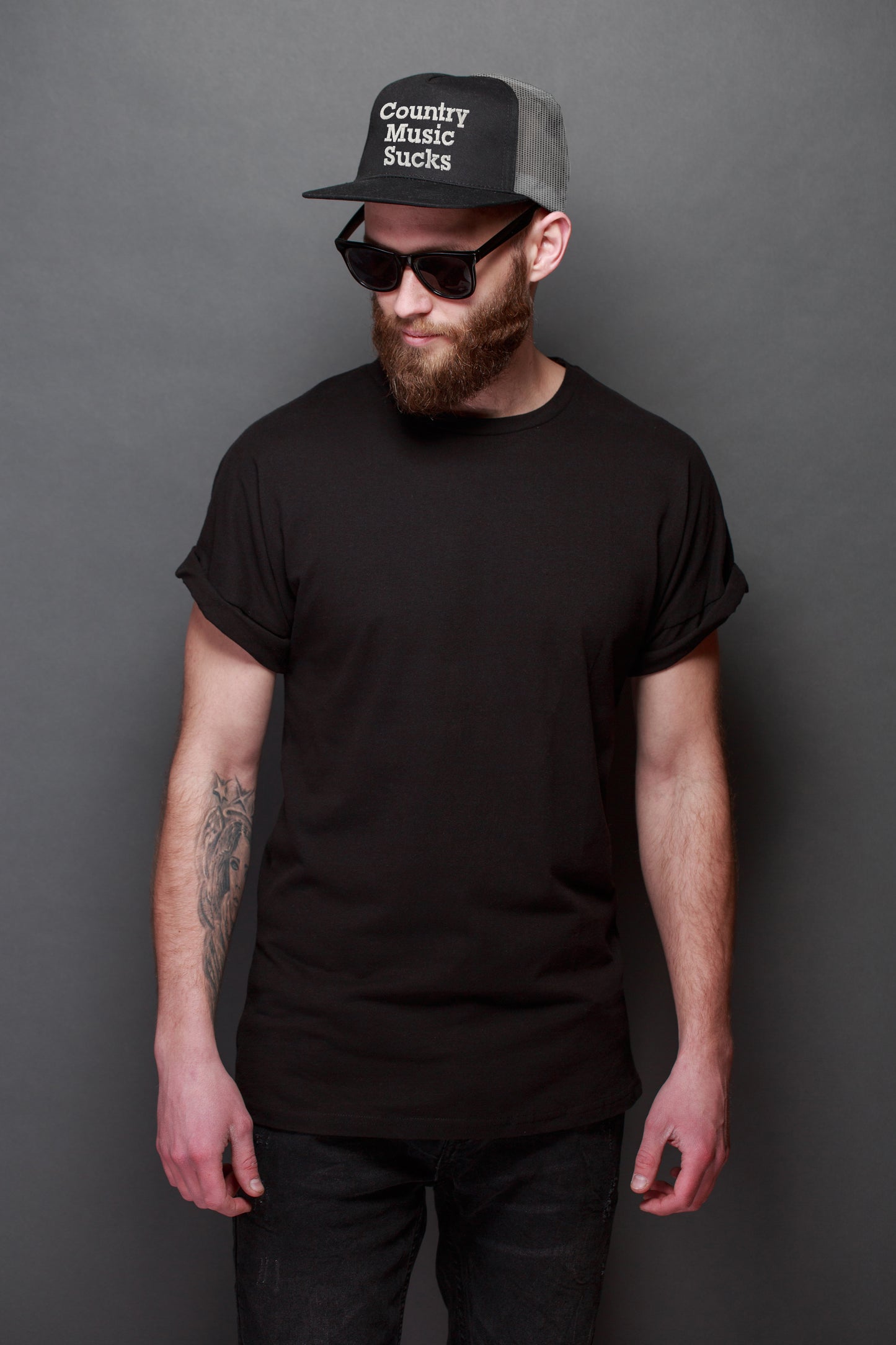 Man wearing a black t-shirt, sunglasses, and a cap with text against a gray background